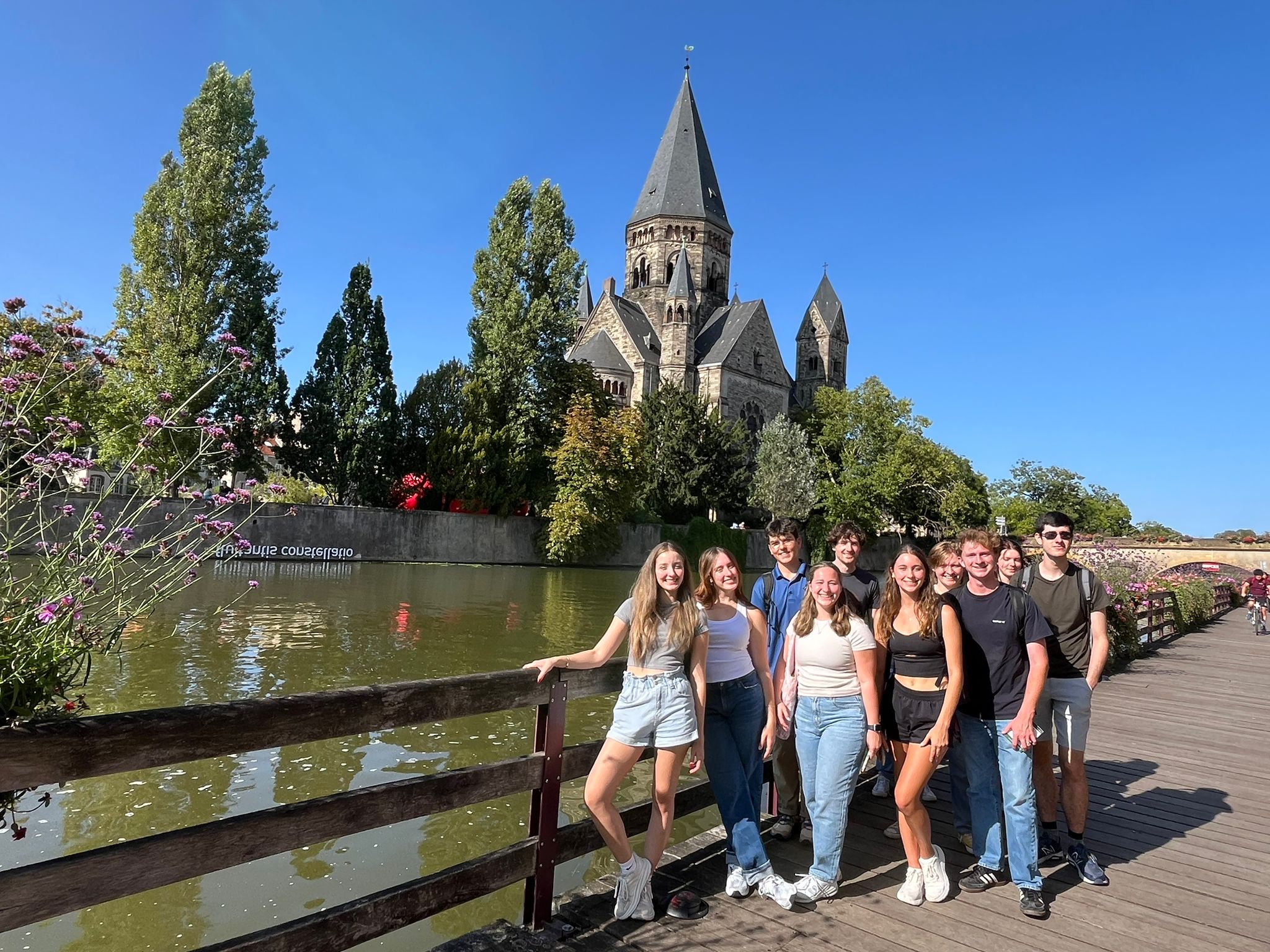 men and women students standing front of a river with a large French cathedral spire in the background